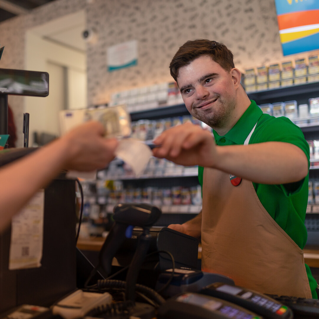 Cheerful young Down Syndrome employee taking cash payment from costumer