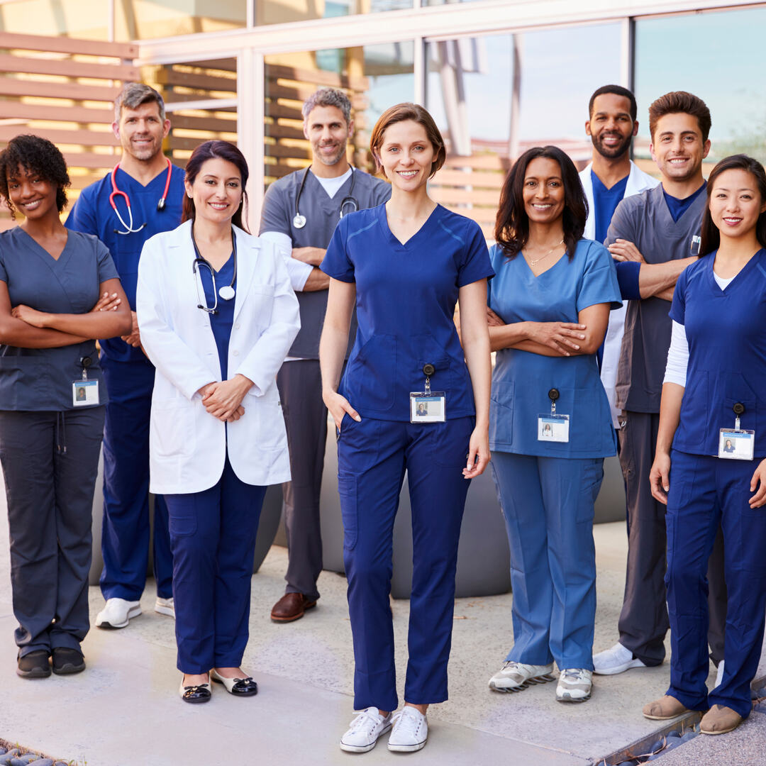 Healthcare team with ID badges stand outdoors, full length